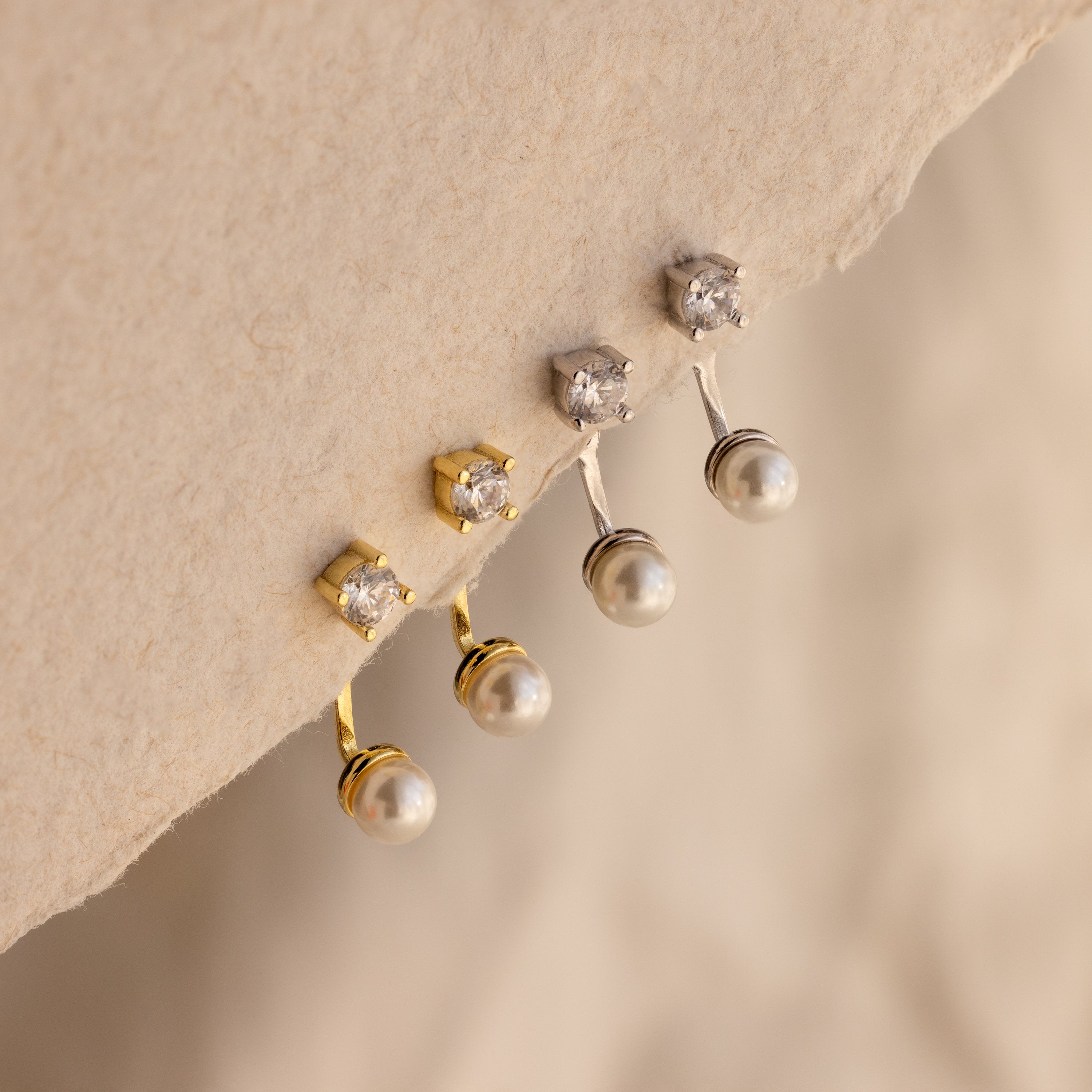 Two pairs of Diamond Pearl Ear Jackets—crafted in gold and silver—showcase sparkling diamonds and pearls, ideal for minimalist jewelry lovers, elegantly displayed on a textured surface.