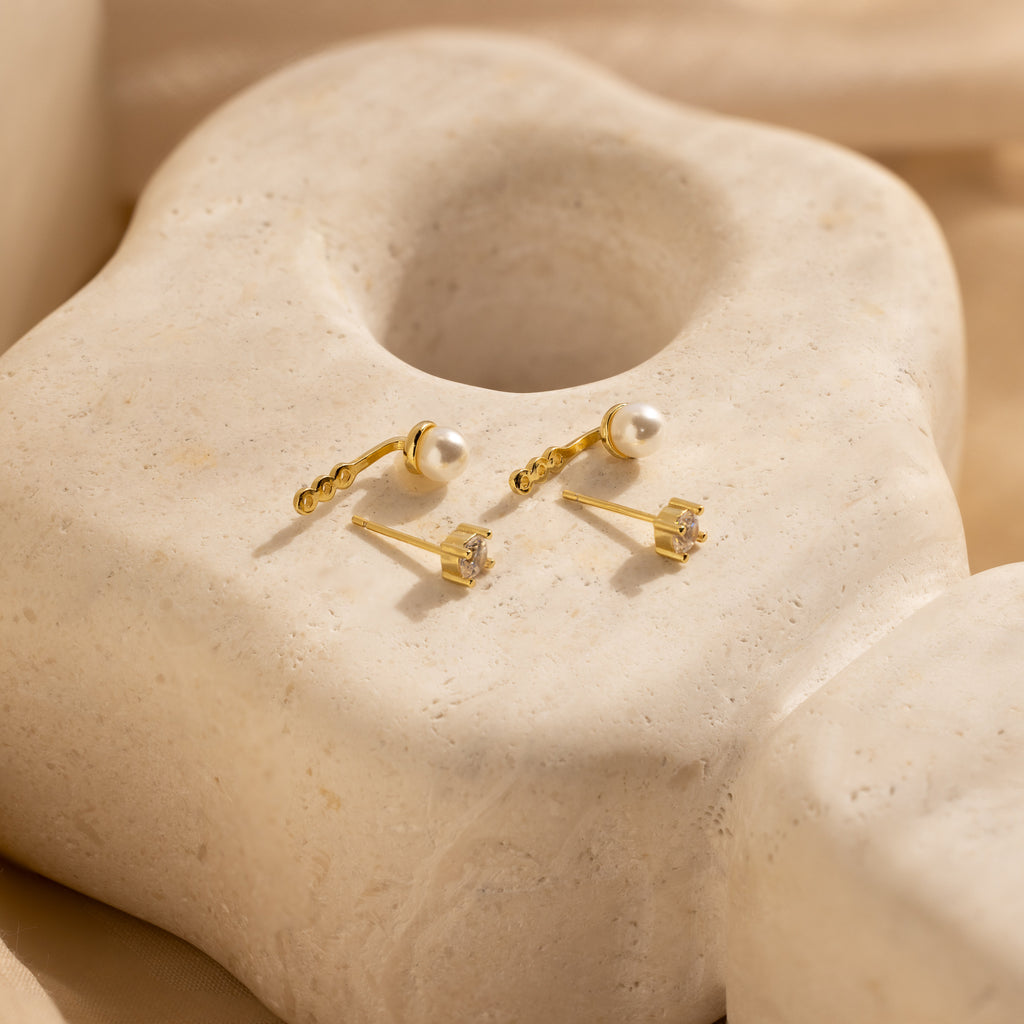 Diamond Pearl Ear Jackets—one featuring a pearl and the other a sparkling diamond—displayed on a textured surface; an ideal choice for minimalist jewelry lovers.