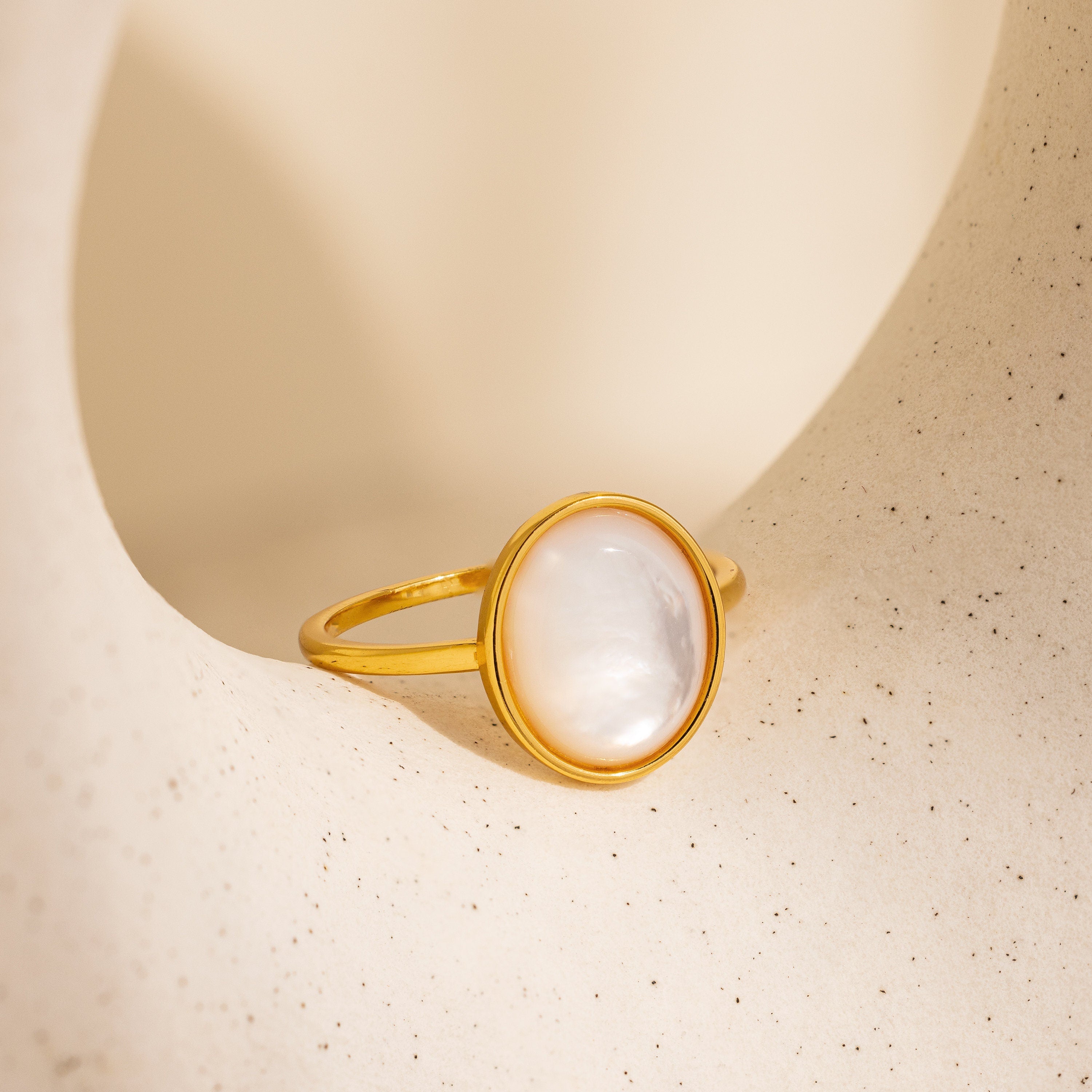 The Mother of Pearl Signet Ring features a vintage-inspired design with a round white pearl set in gold, showcased on a textured beige background.