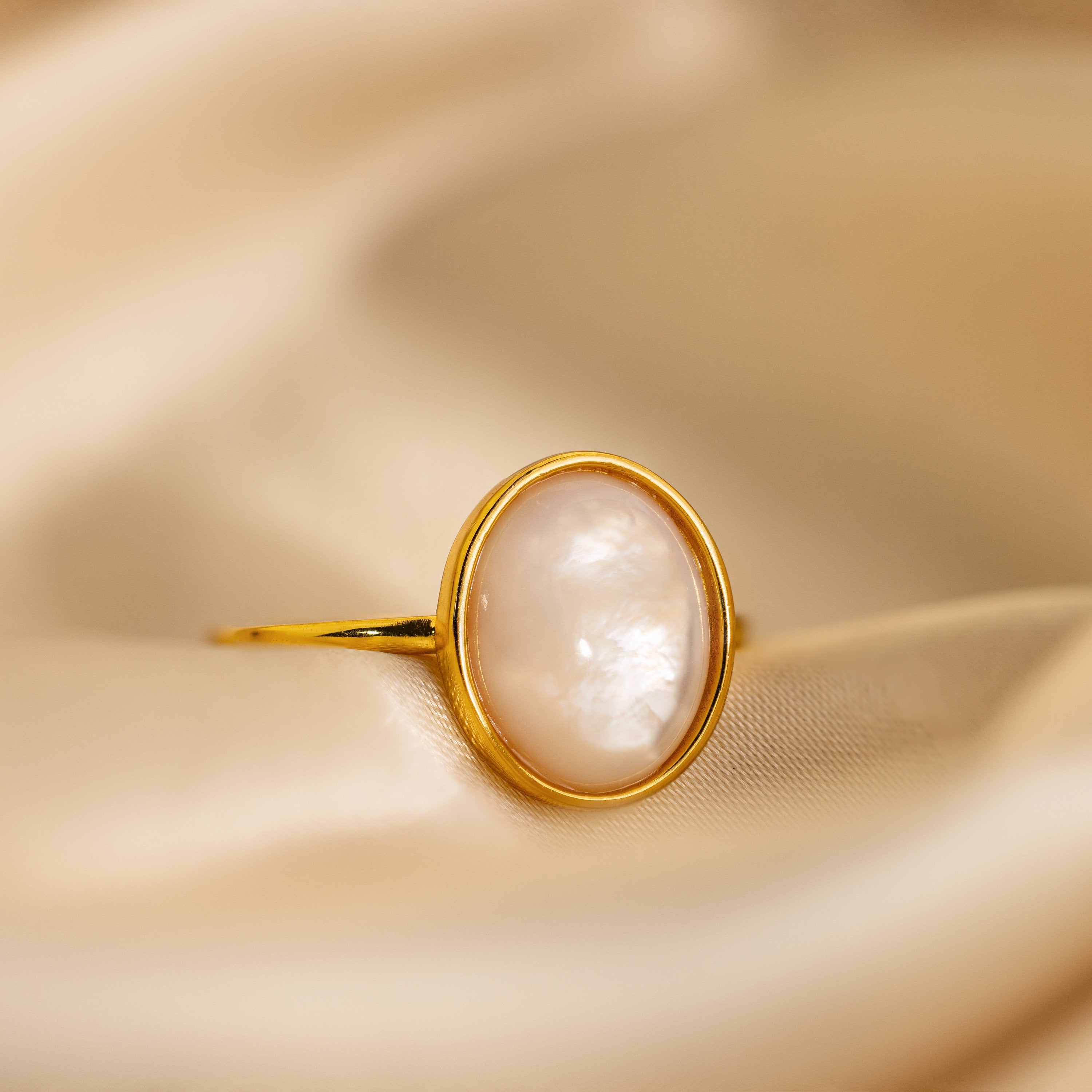 The Mother of Pearl Signet Ring rests on soft beige satin, showcasing vintage-inspired elegance and timeless charm.