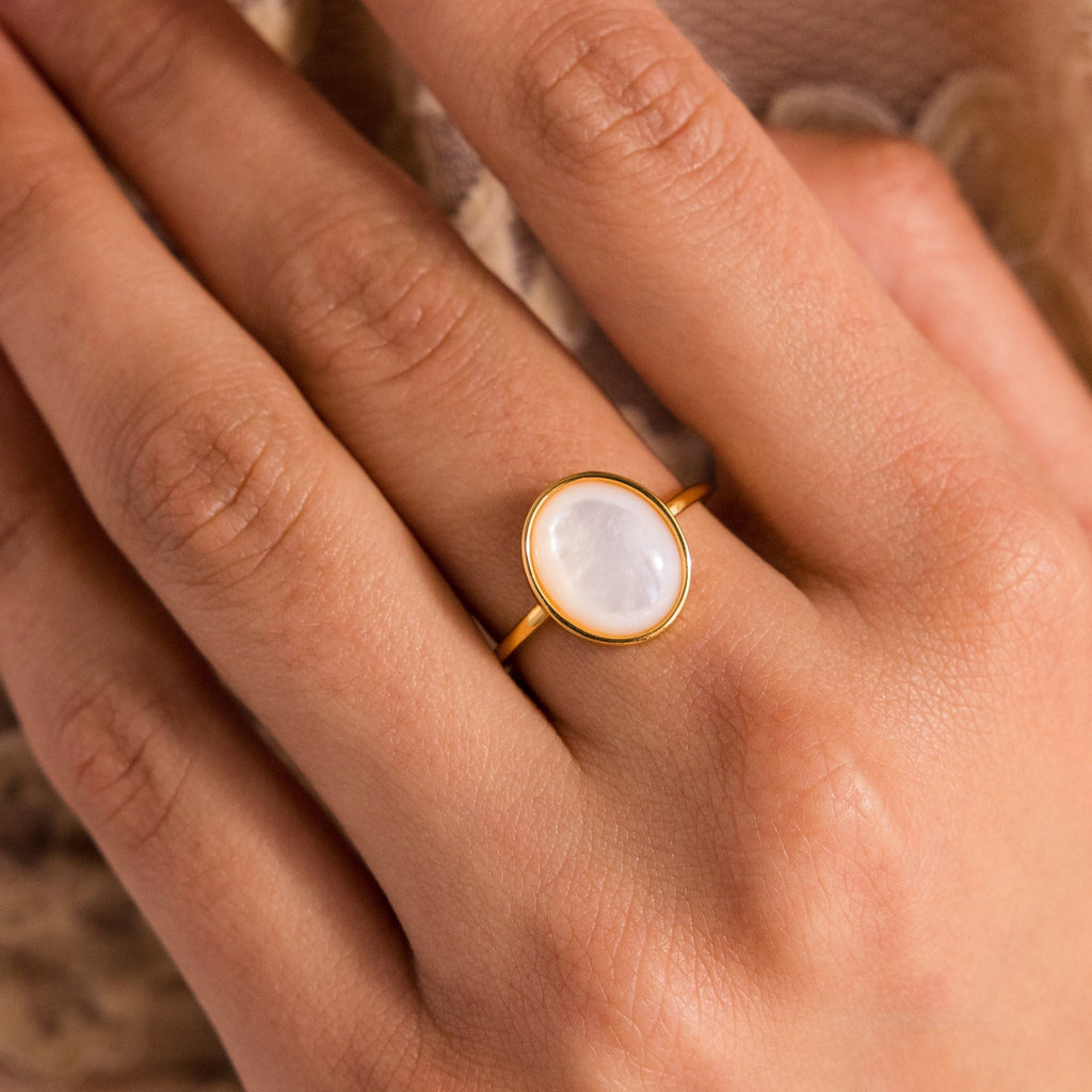 A hand adorned with the Mother of Pearl Signet Ring, featuring a vintage-inspired oval white stone, rests on fabric.