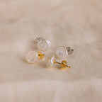 Two pairs of Freshwater Pearl Studs, featuring both gold and silver backs, are displayed on soft beige fabric, showcasing their timeless elegance.
