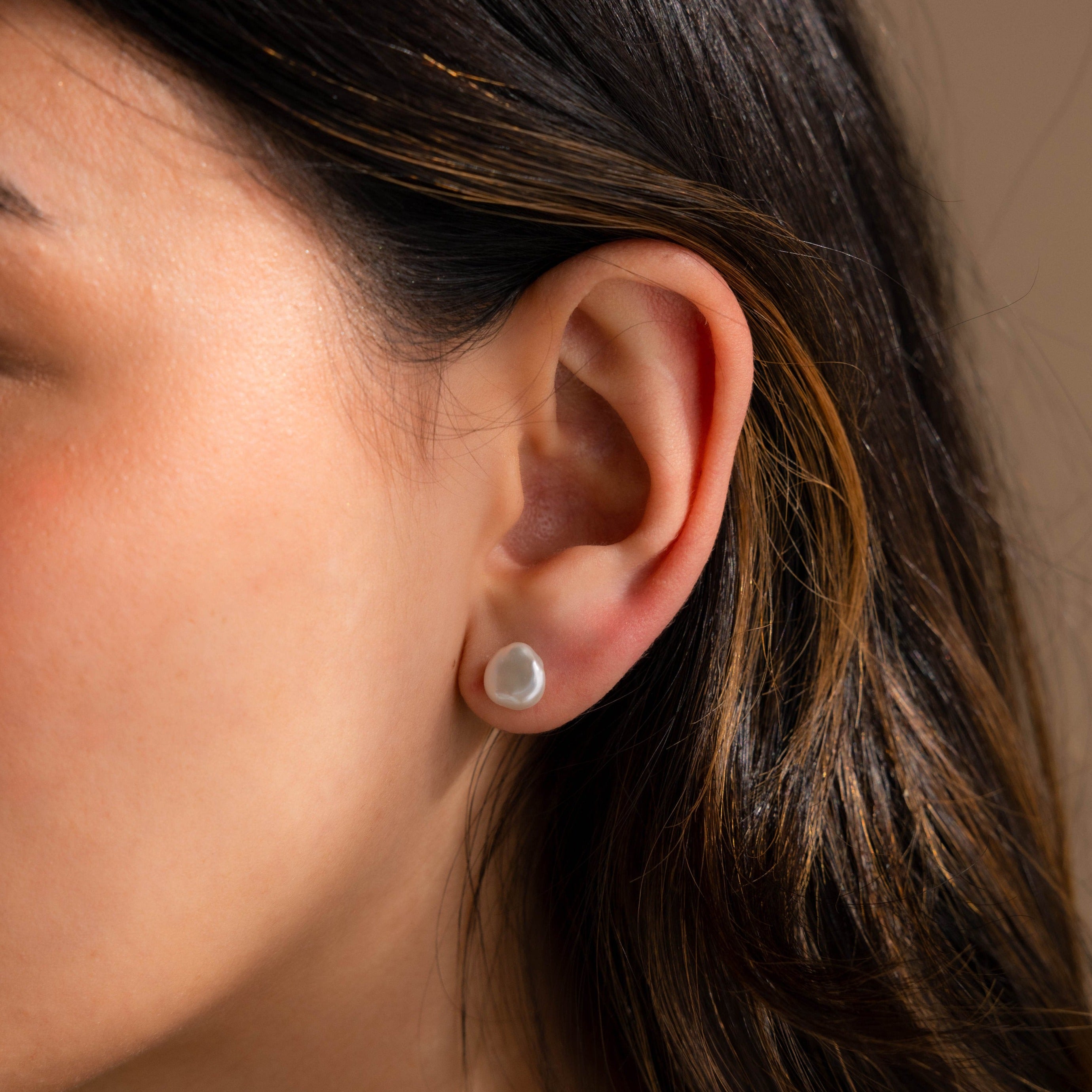 A close-up of a woman’s ear adorned with Freshwater Pearl Studs highlights their timeless elegance against her brown hair and smooth skin.