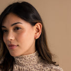 Woman with long dark hair wears a lace top and Pearl Diamond Cluster Huggies, set against a beige background.