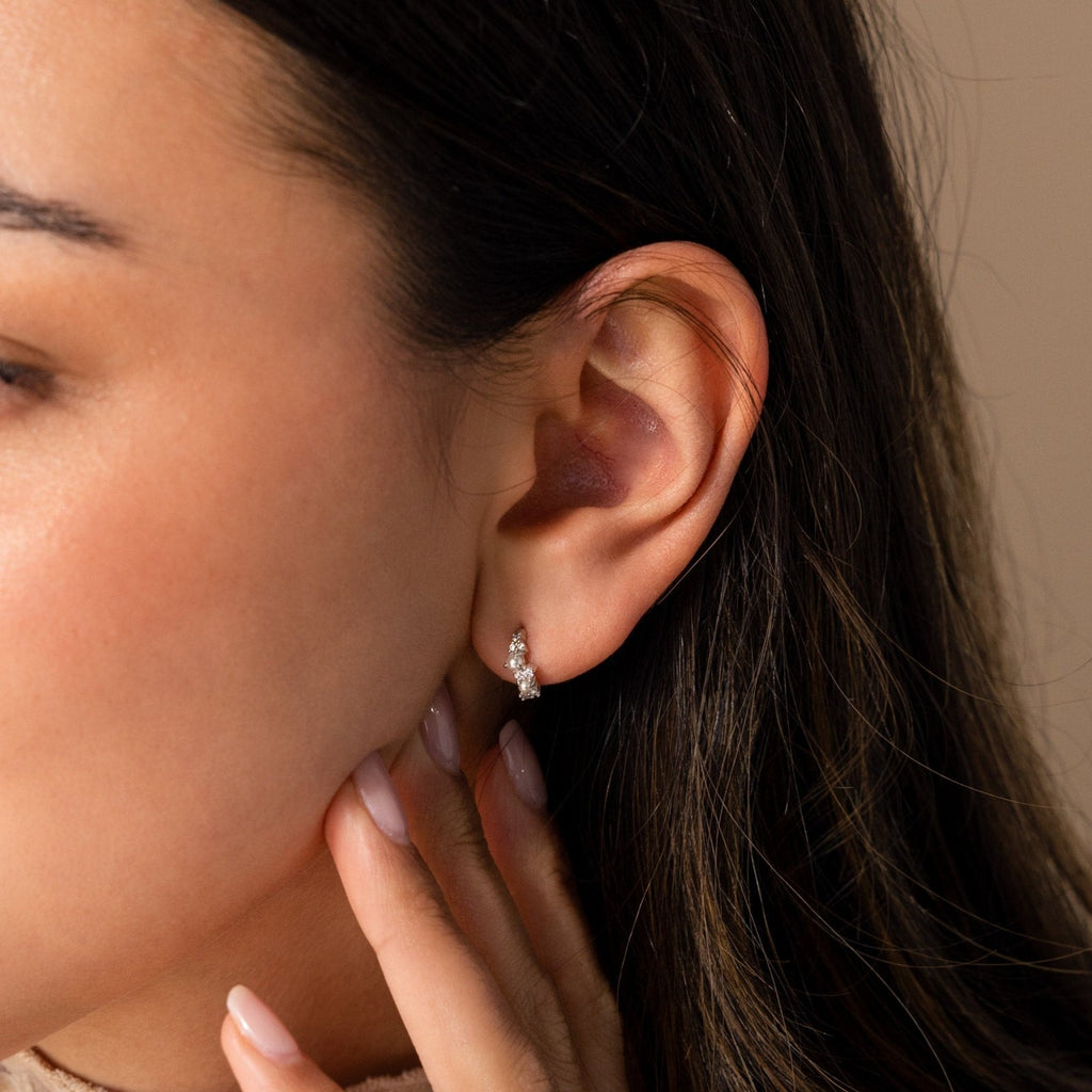 A close-up of a woman's ear adorned with Pearl Diamond Cluster Huggies in Sterling Silver, her hand gently touching her neck.