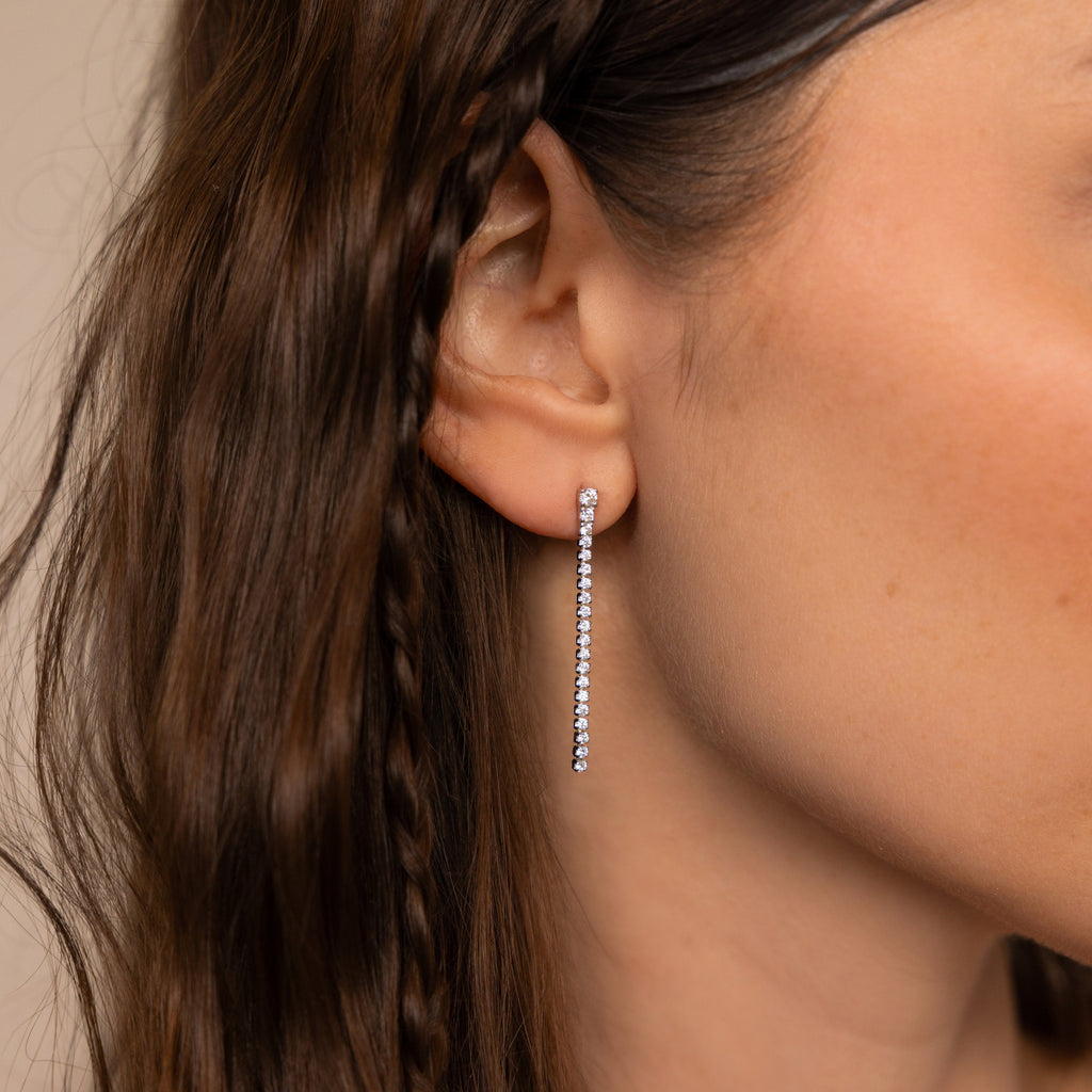 A close-up of a woman’s ear adorned with Diamond Tennis Dangle Earrings, styled with loose and braided hair.