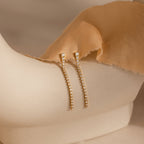 Diamond Tennis Dangle Earrings, featuring rows of sparkling diamonds, are shown on a cream-colored mannequin draped in tan fabric.