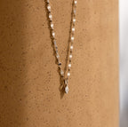 The Dainty Marquise Pendant Necklace, featuring a gold mirror twist chain and small marquise pendant, is displayed against a textured light brown surface.