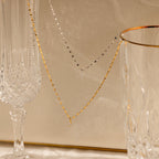 The Dainty Marquise Pendant Necklace is draped over two elegant crystal glasses on a beige background.