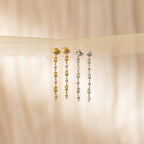 Two pairs of Dainty Diamond Drop Earrings—one gold, one silver—ideal as bridesmaid or wedding jewelry, displayed on sheer beige fabric.