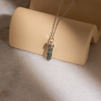 The Agate Quartz Necklace features a marbled green gemstone charm pendant on a silver chain, displayed on a beige curved stand.