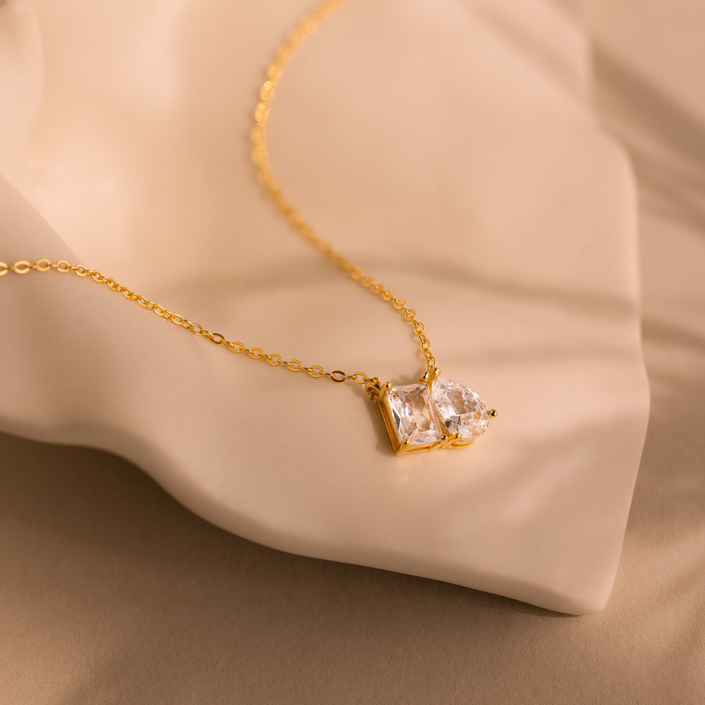Toi et Moi Diamond Necklace featuring an emerald cut diamond pendant sparkling on a soft beige fabric background.