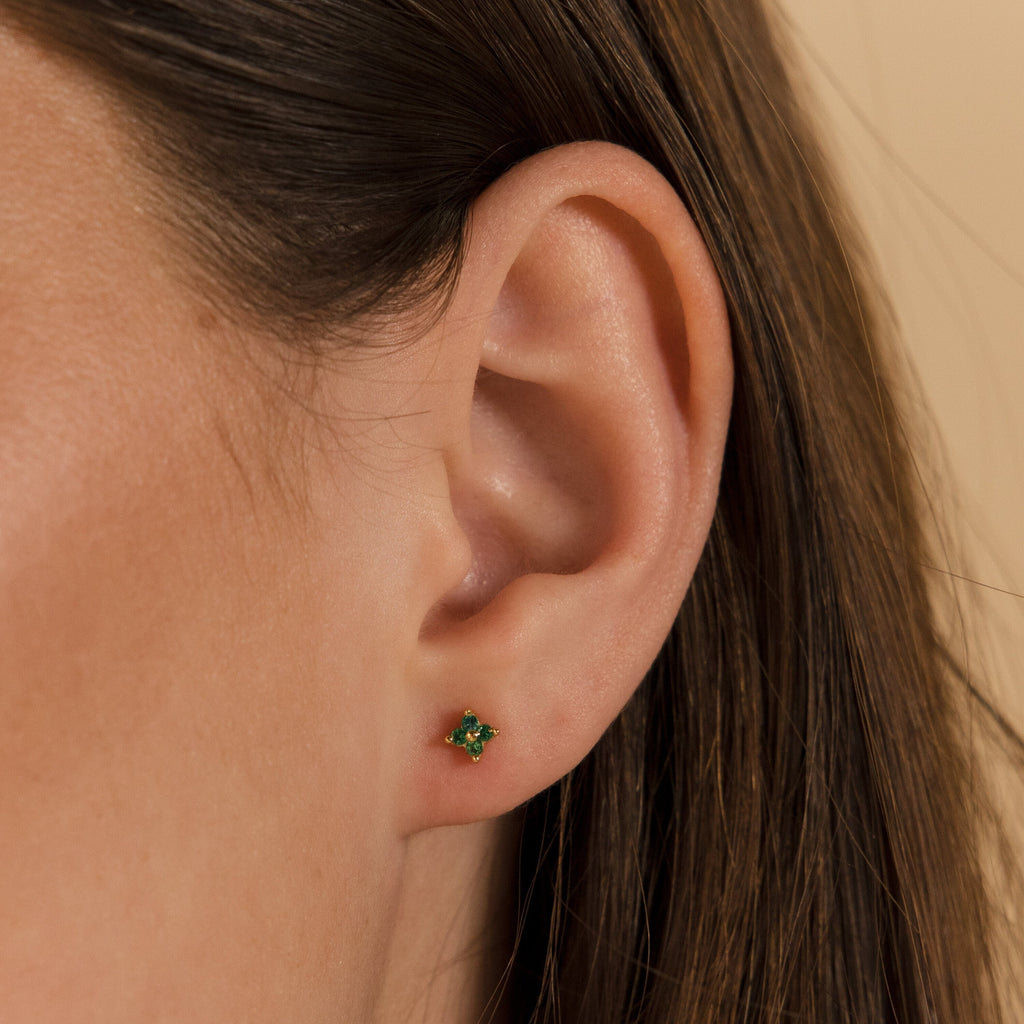 Close-up of a woman's ear wearing Emerald Ivy Flower Studs, with brown hair partially visible.
