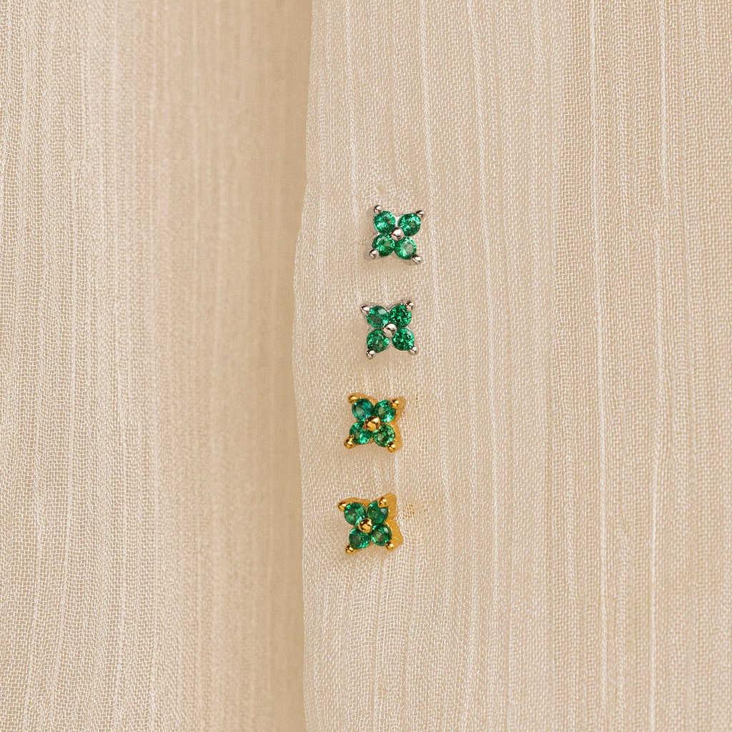 Four pairs of small green gemstone earrings—two silver and two gold—are displayed on beige fabric. The nature-inspired Emerald Ivy Flower Studs add a touch of elegance to any look.