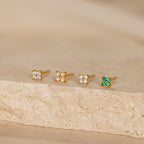 A row of Emerald Ivy Flower Studs sits gracefully on white stone, showcasing nature-inspired jewelry at its finest.