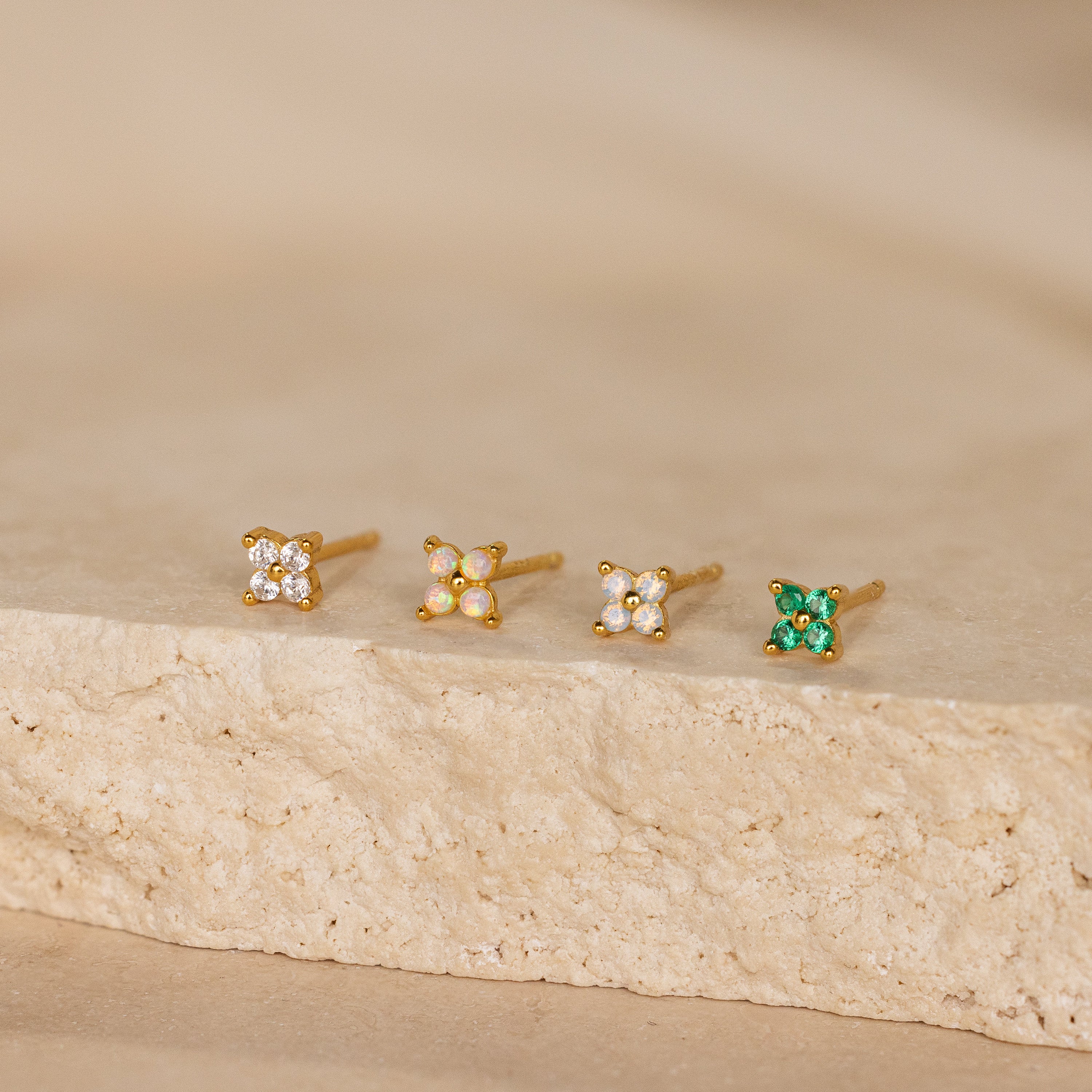 A row of Emerald Ivy Flower Studs sits gracefully on white stone, showcasing nature-inspired jewelry at its finest.