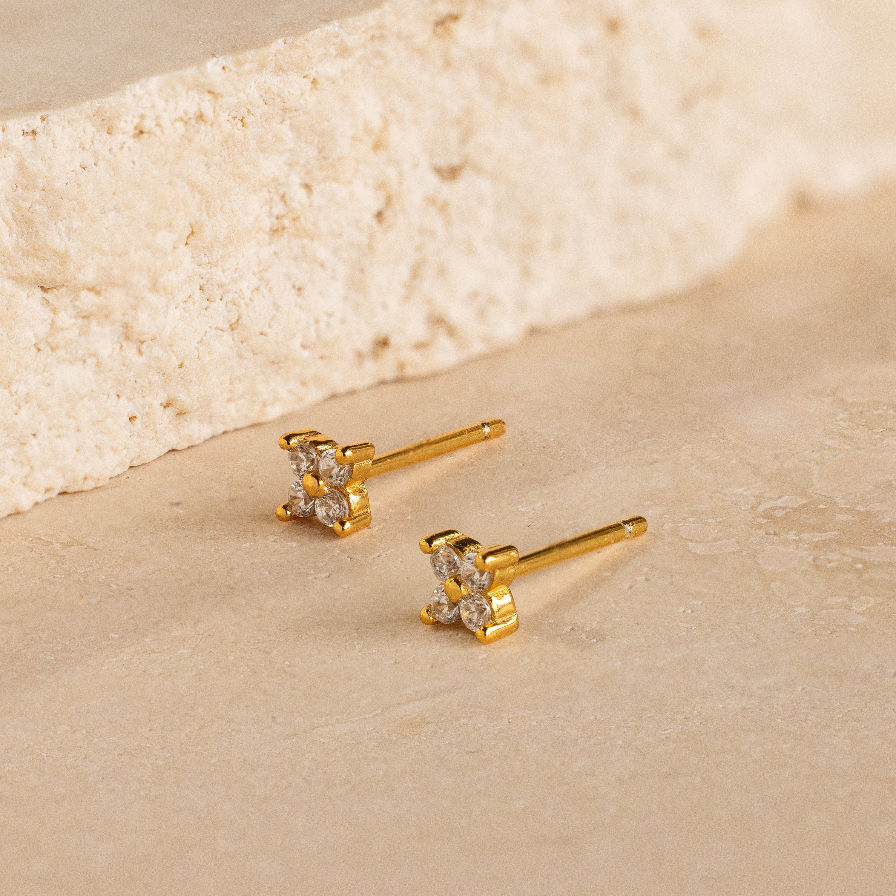 Diamond Ivy Flower Studs with clear gemstones rest on a beige stone surface, offering a versatile accessory ideal for weddings or adding everyday elegance.