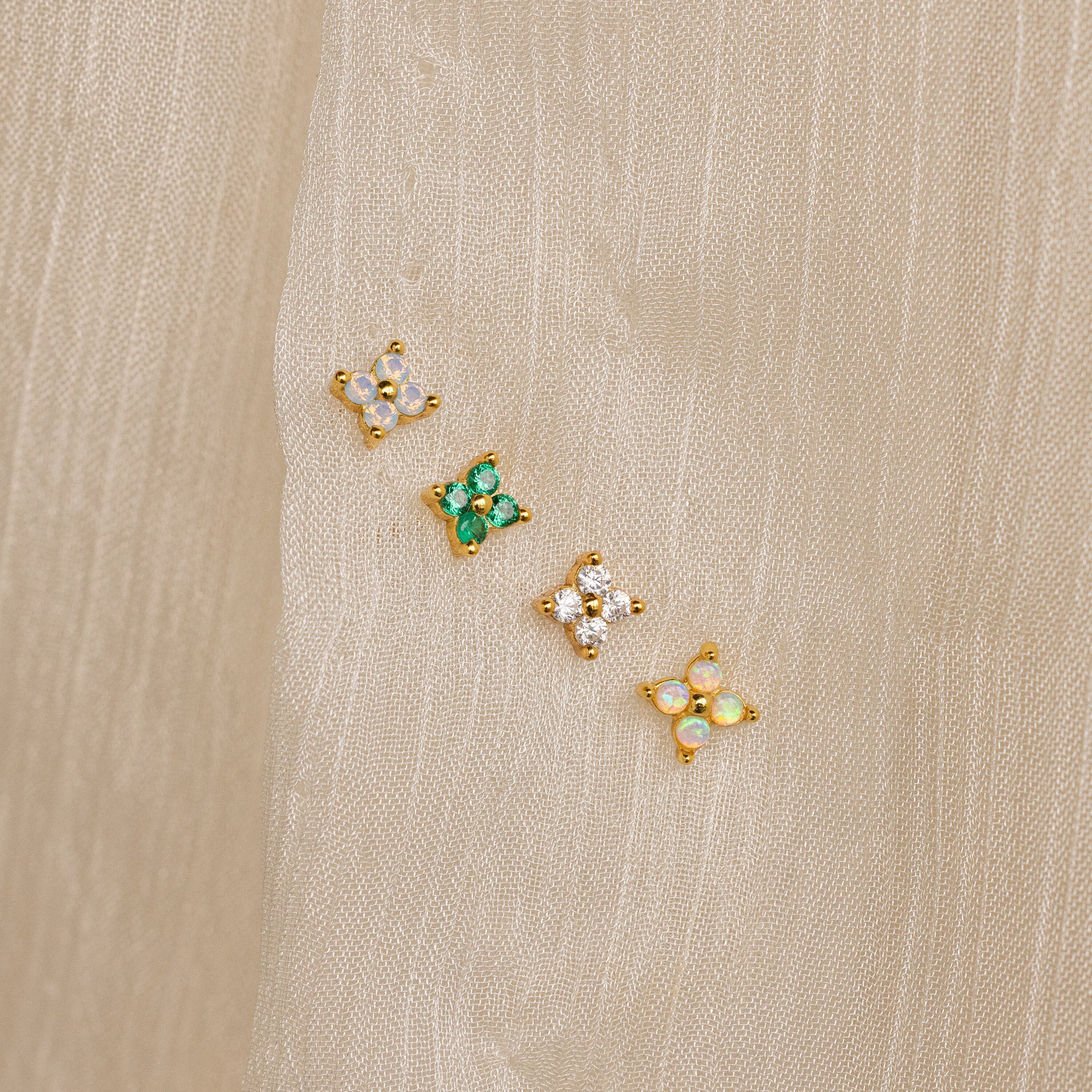 Diamond Ivy Flower Studs—small, gold floral earrings with colorful stones—are displayed on beige fabric and make a versatile accessory, perfect as wedding earrings or for any special occasion.