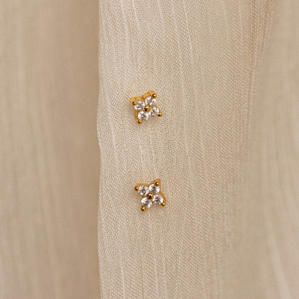The Diamond Ivy Flower Studs, ideal for weddings or everyday wear, are shown in pairs on a cream-colored textured fabric background.