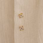 The Diamond Ivy Flower Studs, ideal for weddings or everyday wear, are shown in pairs on a cream-colored textured fabric background.