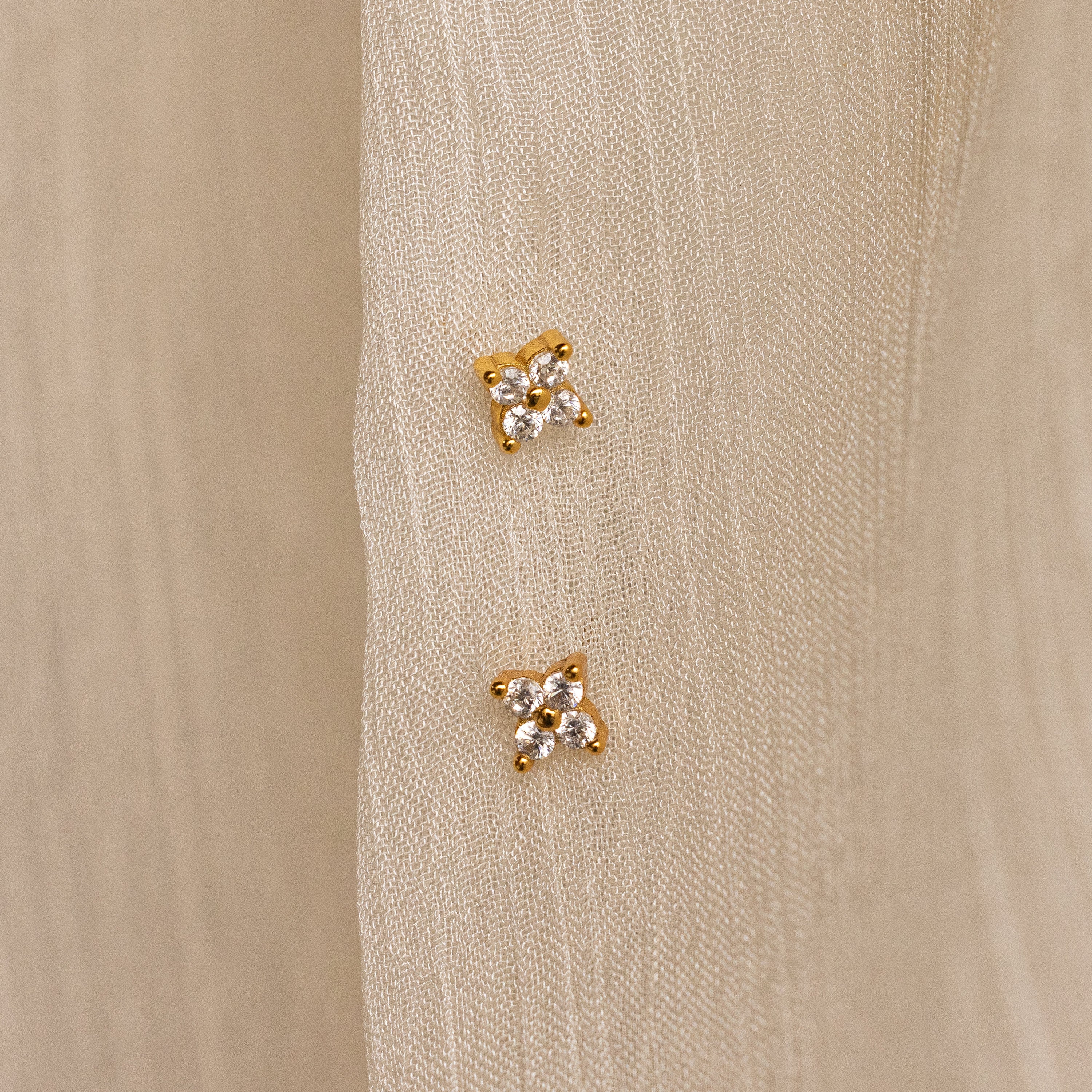 The Diamond Ivy Flower Studs, ideal for weddings or everyday wear, are shown in pairs on a cream-colored textured fabric background.