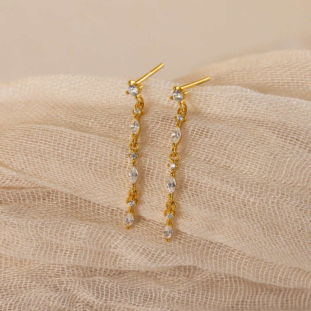 Dainty Diamond Drop Earrings, ideal for weddings or bridesmaids, featuring sparkling crystals and displayed on a soft beige textured fabric background.