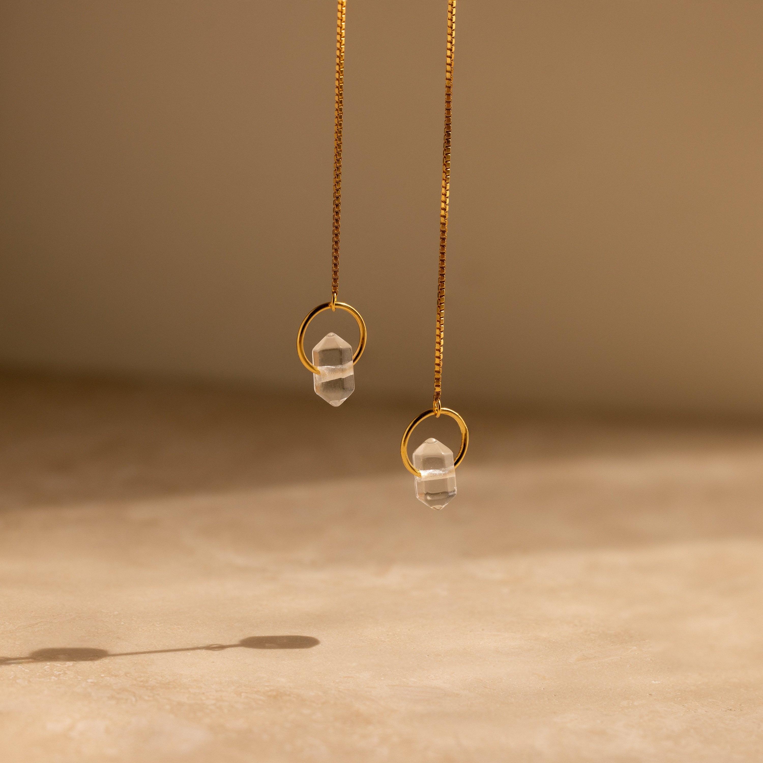 Herkimer Diamond Earrings featuring gold threader design with clear glass stone pendants, photographed on a soft beige background.