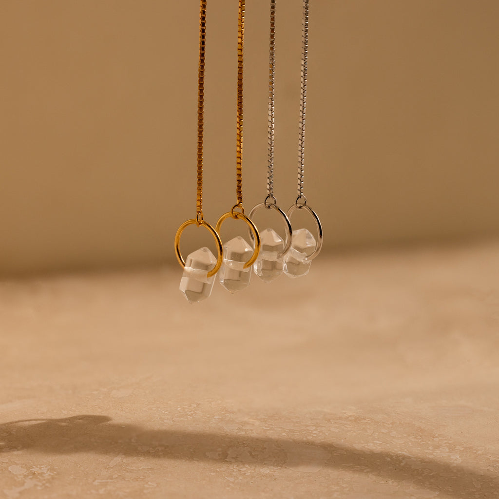 Herkimer Diamond Earrings shine against a neutral beige background, their crystal brilliance reminiscent of elegant pendant necklaces paired with glass stone studs.