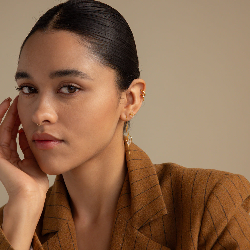 A woman with slicked-back hair wears a brown pinstripe blazer and the Herkimer Diamond Earrings, resting her hand on her face.