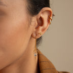 Close-up of a woman's ear with three gold earrings, featuring Herkimer Diamond Earrings and studs, styled with a brown checked blazer.