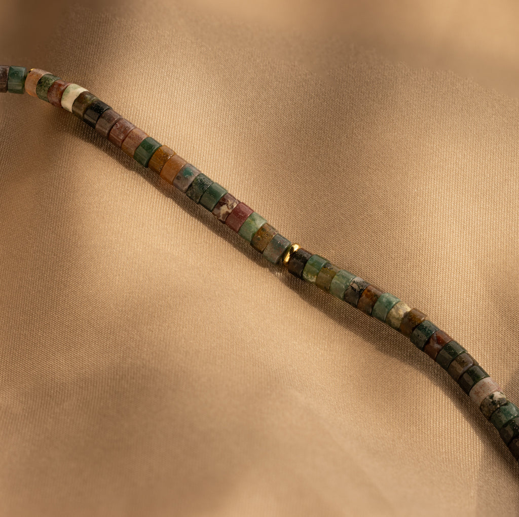 The Moss Agate Beaded Necklace, with its mixed color beads, is displayed on light brown fabric, showcasing natural and earthy elegance.