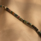 The Moss Agate Beaded Necklace, with its mixed color beads, is displayed on light brown fabric, showcasing natural and earthy elegance.