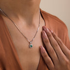 A woman wearing the Vintage Emerald Pendant Necklace and a brown satin top gently touches her collarbone.