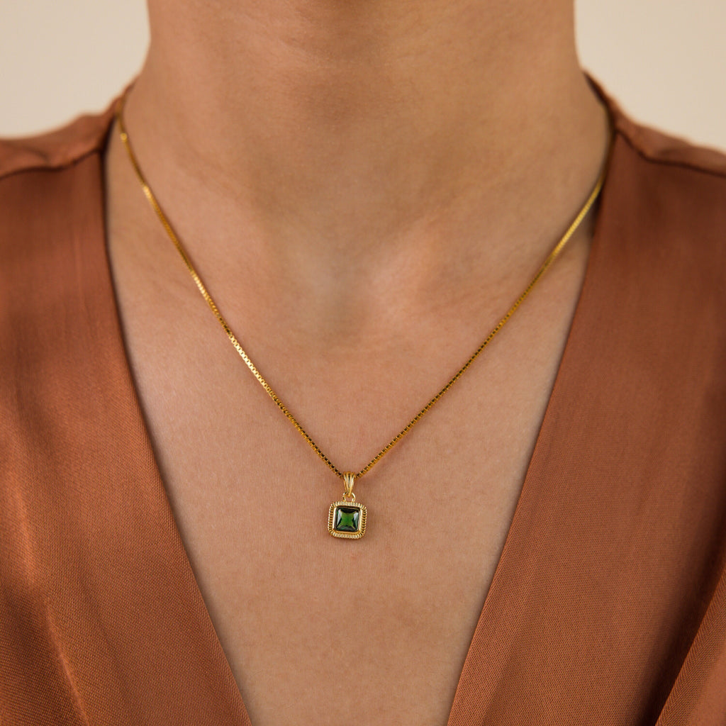 The Vintage Emerald Pendant Necklace is styled over a brown V-neck top.