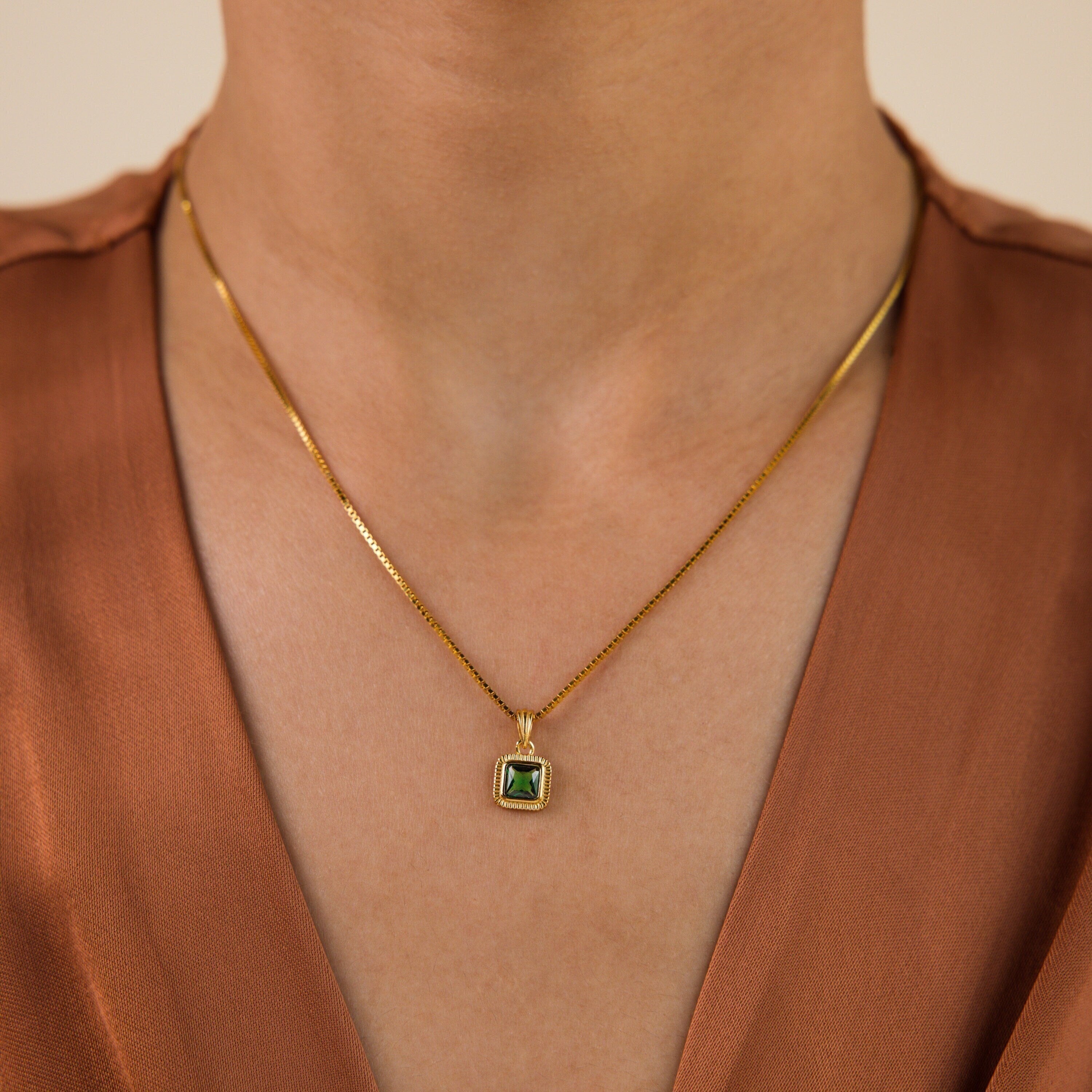 The Vintage Emerald Pendant Necklace is styled over a brown V-neck top.