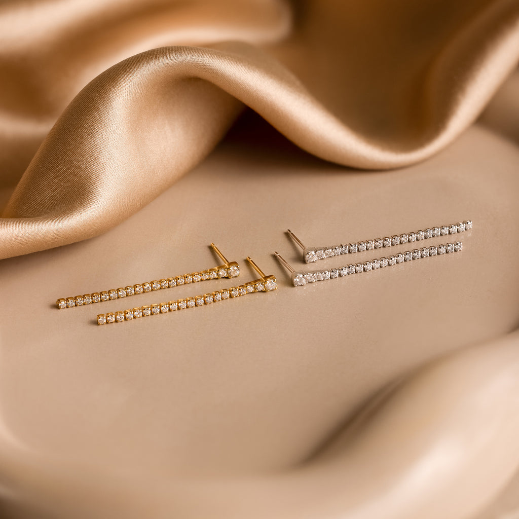 The Diamond Tennis Dangle Earrings glimmer with sophistication, showcasing timeless style in a pair of elegant gold diamond earrings.