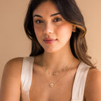 A woman with wavy hair in a cream top layers gold necklaces—one reading JASMINE, another with a flower pendant—and finishes her look with the elegant Interlocking Pearl Necklace.
