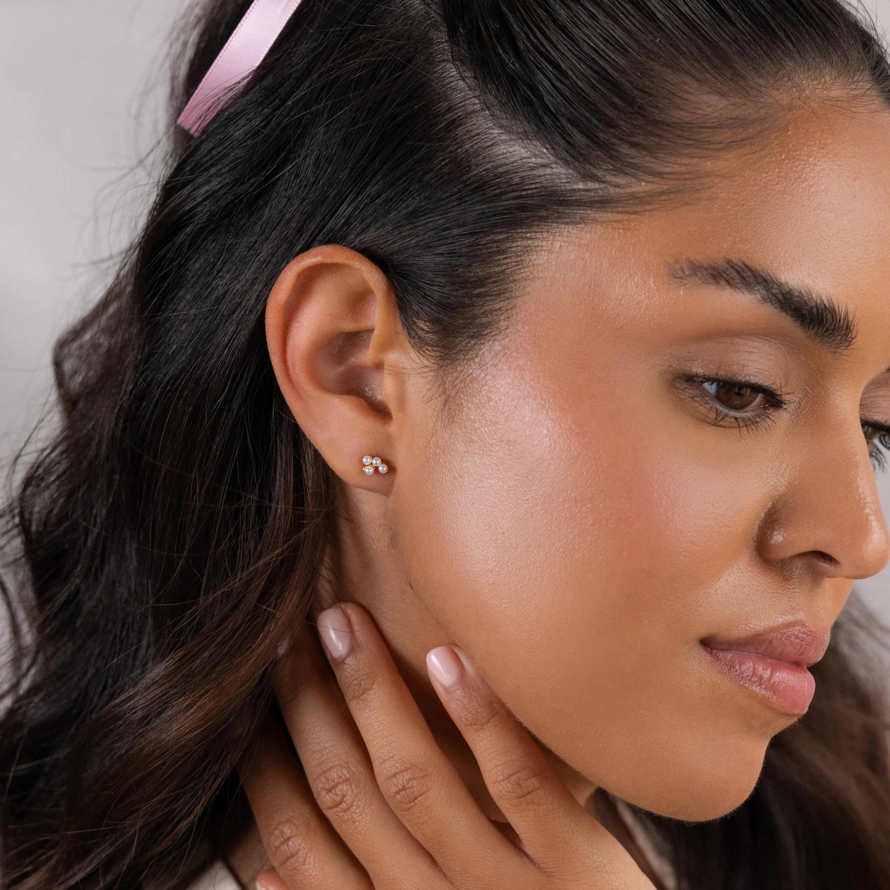 A woman with long brown hair and a pink hairpin wears Pearl Cluster Drop Studs—an elegant choice that makes the perfect wedding accessory.