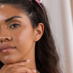 A woman with long dark hair wears the Pearl Bar Chain Studs, touching her chin as she looks at the camera.