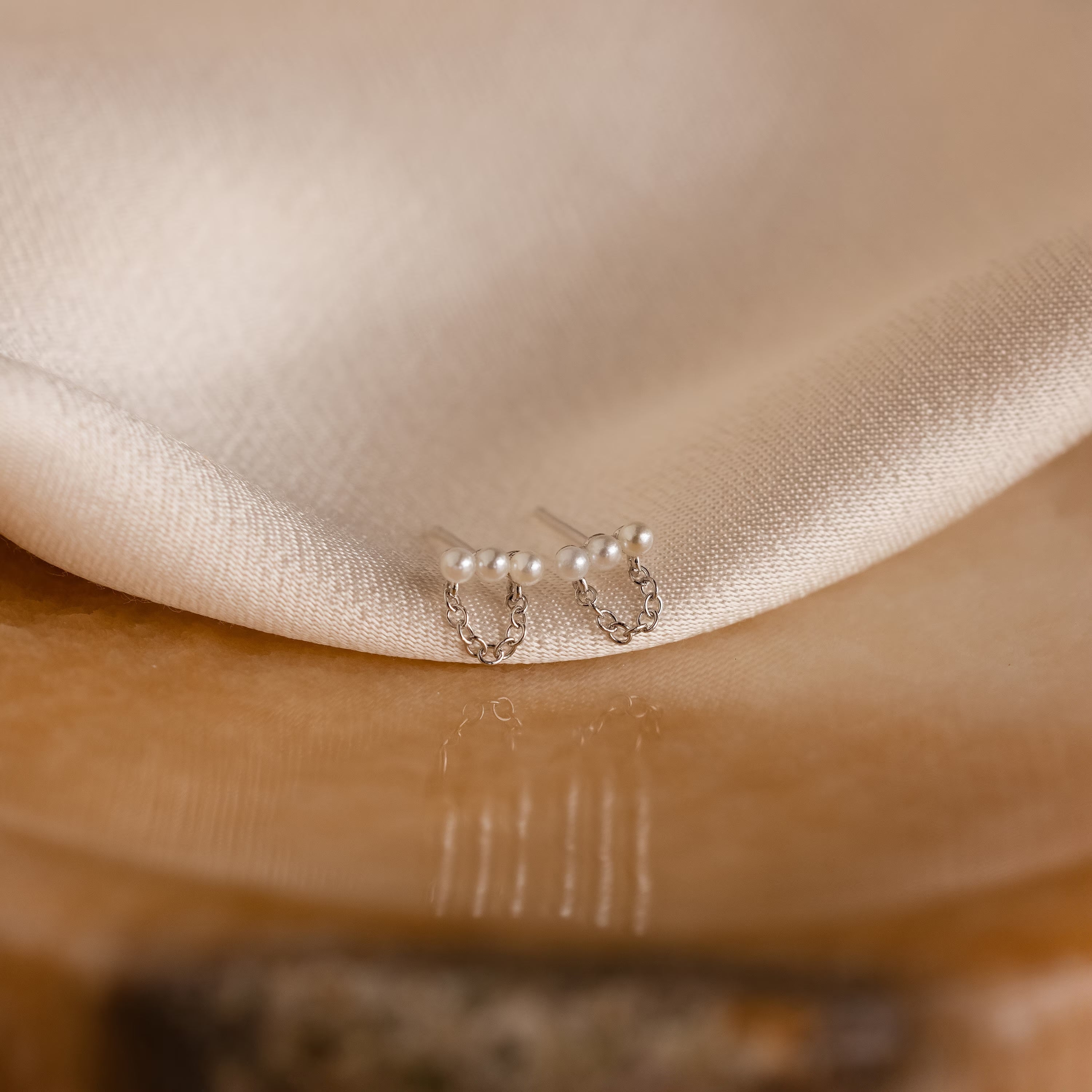 Pearl Bar Chain Studs rest on a soft, light beige fabric, adding a touch of elegant coquette style to any look.
