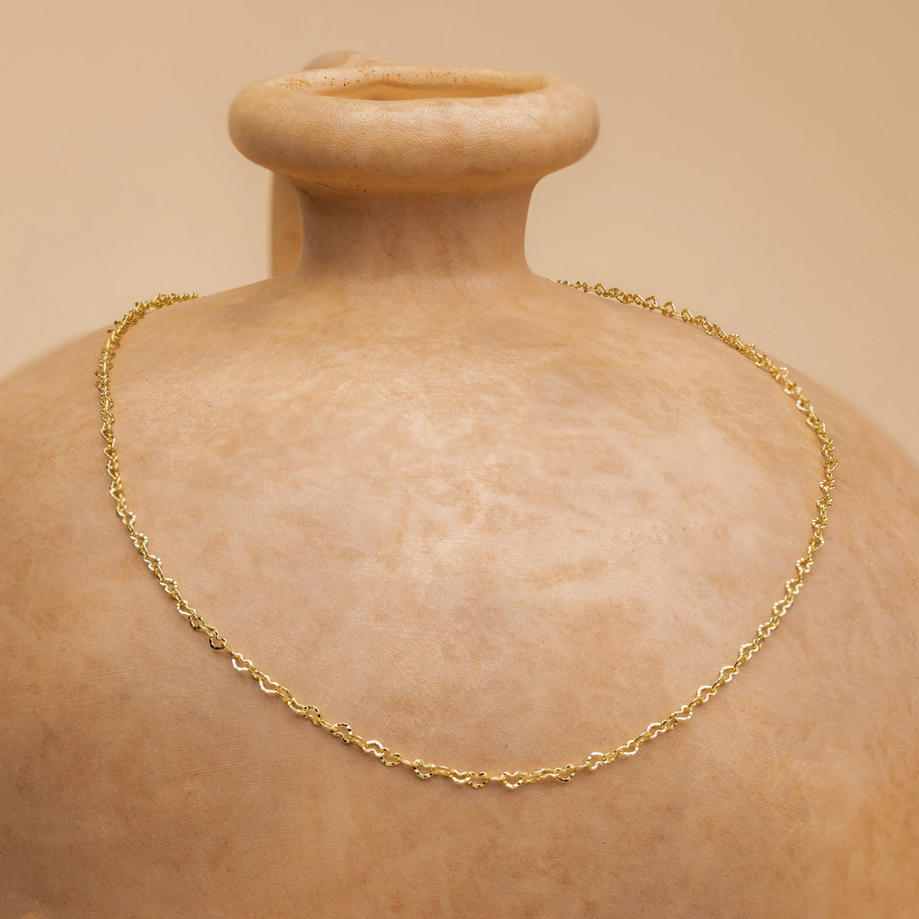The Heart Link Chain Necklace, featuring interlocking hearts, is draped over a beige ceramic vase for a subtle romantic accent.