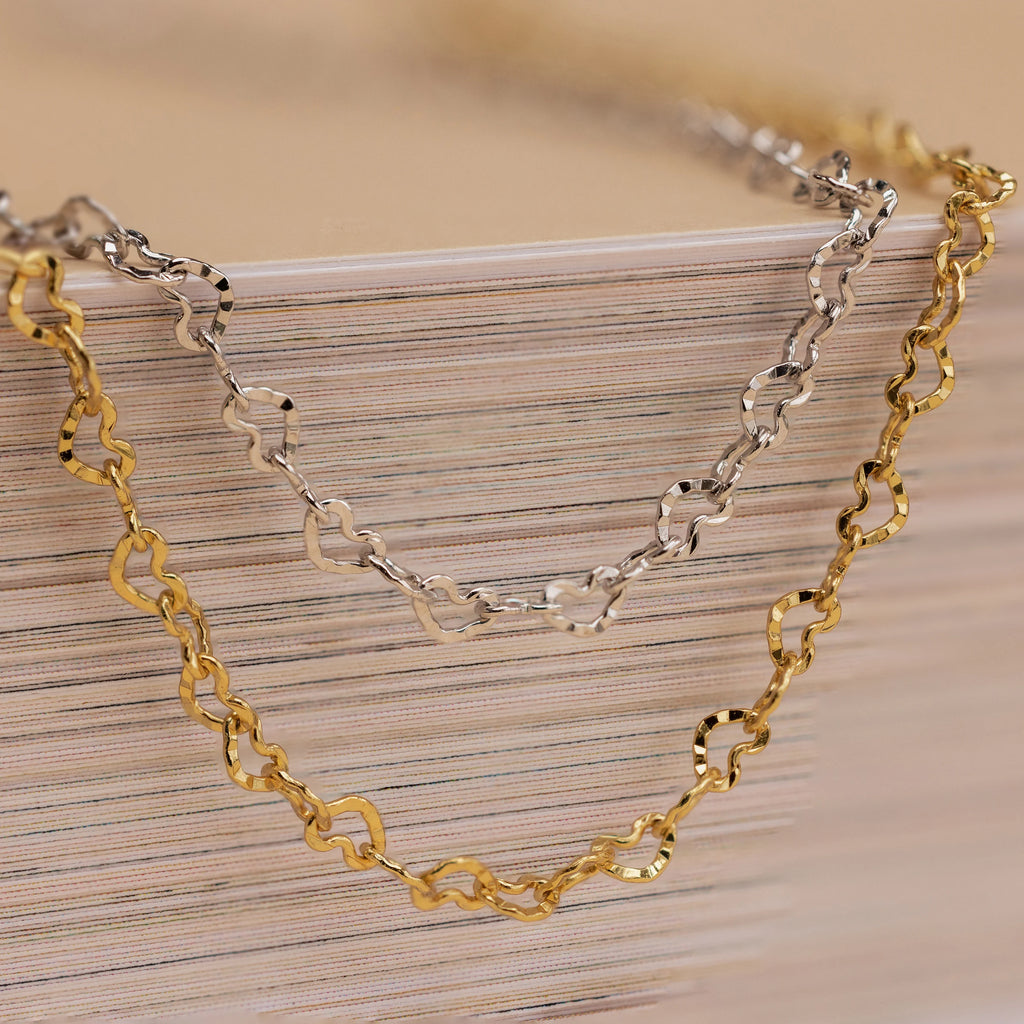 Heart Link Chain Necklaces in gold and silver with interlocking hearts are displayed draped over stacked books, creating a romantic accent.