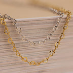 Heart Link Chain Necklaces in gold and silver with interlocking hearts are displayed draped over stacked books, creating a romantic accent.