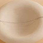 The Heart Link Chain Necklace, featuring interlocking hearts on a delicate silver chain, is displayed on a smooth, round, off-white ceramic dish.