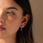Close-up of model wearing silver huggie earrings with a dangling pearl charm.