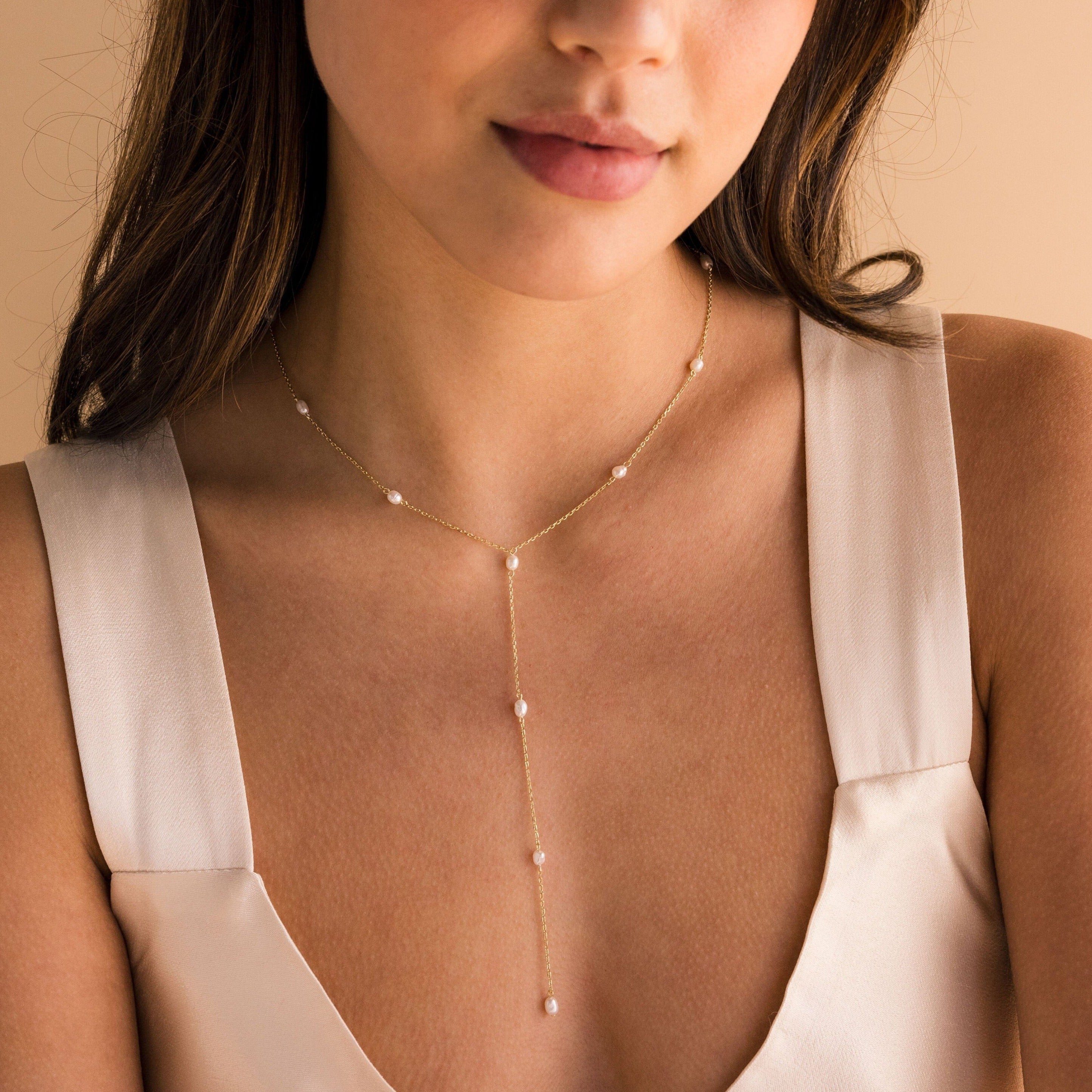 Woman wearing a cream dress and a delicate gold Pearl Station Lariat Necklace adorned with small pearl charms.