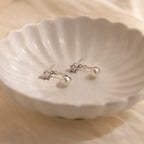 A pair of Diamond Pearl Ear Jackets rests on a white, scalloped dish—perfect for minimalist jewelry lovers.