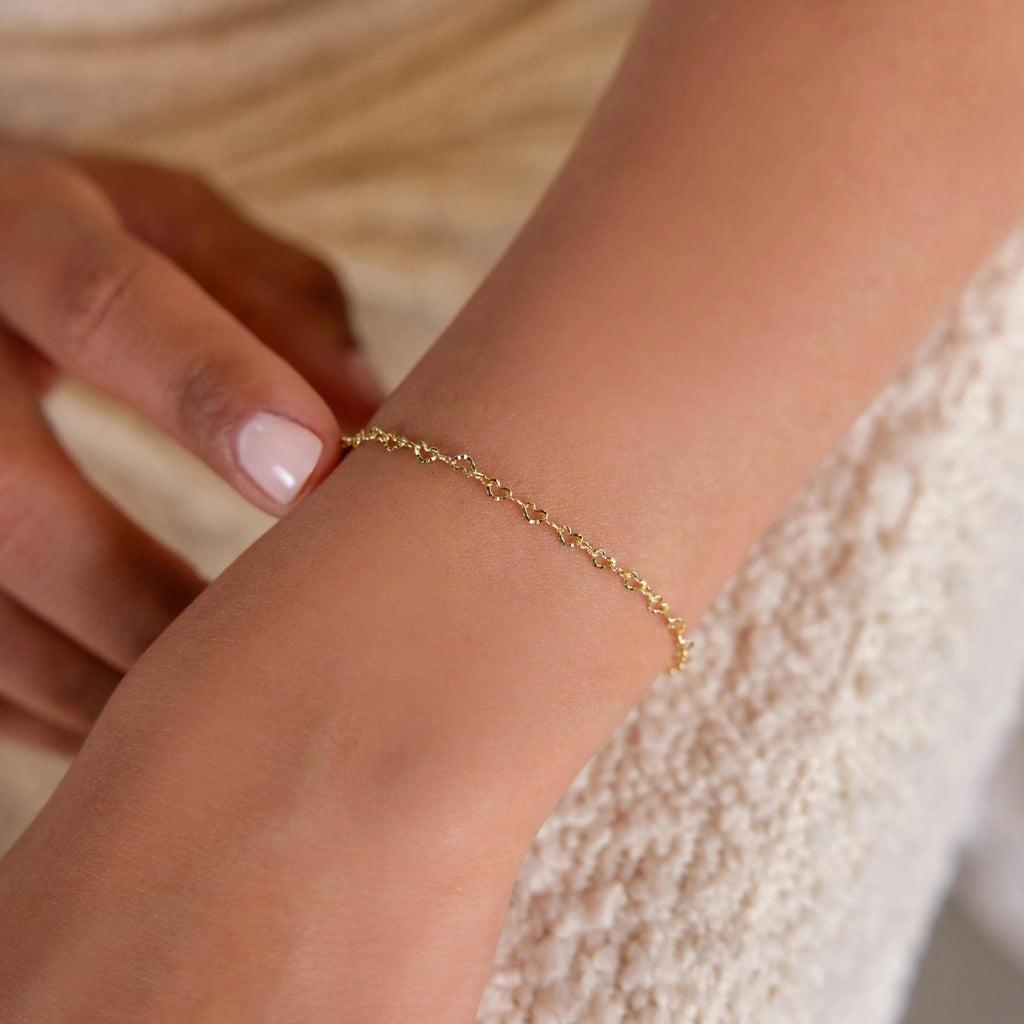 Wearing the Heart Link Chain Bracelet, a person gently touches their wrist, showcasing the romantic elegance of this delicate jewelry.