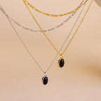 The Onyx Figaro Duo Necklace set features four layered chains—two gold, two silver—with sleek black onyx pendants and classic Figaro links, styled together and displayed on a beige background.
