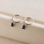 Onyx Baguette Drop Huggies featuring silver hoops with small rectangular onyx stone charms, displayed on a cream fabric surface.
